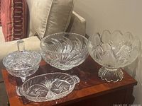 Four pieces of vintage cut glass crystalware on wooden table: lidded bowl, divided tray, round bowl, and floral bowl.
