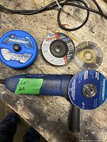 Angle grinder placed on a workbench with cut off wheels nearby, showing grinder body and wheel types.