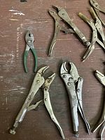Top view of 10 hand tools laid out on wooden surface showing variety of adjustable wrenches and locking pliers.