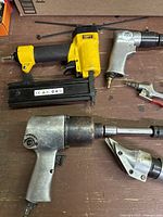 Photo of yellow and black pneumatic brad nailer, silver impact wrench, and a nibbler with a flat metal attachment.