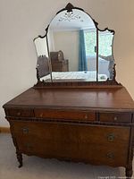 Front view of antique wooden dresser with large ornate mirror, three small drawers and two large drawers beneath. Shows decorative handles and carved wood details.
