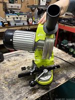 Front side view of green electric chain sharpener showing motor, black handle and mounting clamp.