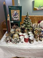 Wide shot showing assortment of Christmas mugs, snow globes, tabletop fountains, ceramic tree and various decorations