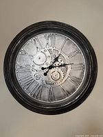 Full view of the steampunk wall clock showing the circular black frame and metallic gear design face with Roman numerals.