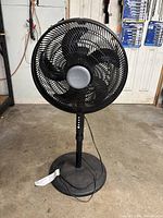 Full view of the black Comfort Mate floor fan showing the circular grille, three-blade fan, stand, and base.