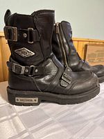 Side angle view showing Harley Davidson logo plate, two adjustable buckles, zipper and stitching on leather boot.