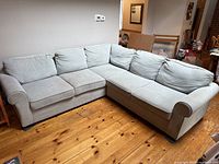 Full view of light gray modern sectional sofa with rolled arms and plush back cushions arranged in L shape on wooden floor.