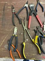 Photo showing a variety of pliers, bolt cutters, and wire cutters of different sizes and handle colors laid out on a wooden surface.
