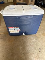 Front view of Rubbermaid cooler showing blue body, white lid with cup holders, and front spigot.