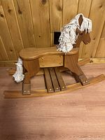 Side view of small wooden rocking horse, showing white yarn mane and tail and polished wooden finish.