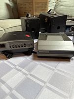 Multiple vintage cameras including Polaroid Spectra System in foreground with black and silver body, older box cameras with leather cases in background.