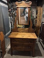 Full front view of the wood dresser showing two drawers and attached framed swivel mirror with decorative carved wood top.