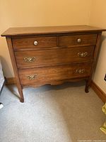 Front view of wooden dresser showing two small top drawers with round knobs and two larger bottom drawers with brass handles.