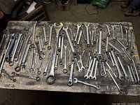Wrenches laid out on wooden table showing a large assortment of various sizes and brands.