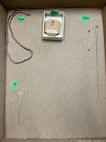 Overview of all jewelry items in lot laid out in a cardboard box with small green labels for metal types
