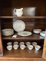 Full tea set displayed in a wooden cabinet showing dinner plates, luncheon plates, cups, saucers, and creamer.