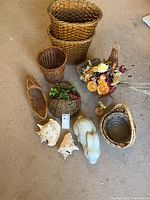 View of entire lot showing nine woven baskets, floral arrangement in one basket, concrete bunny statue, and two large seashells on beige carpet.