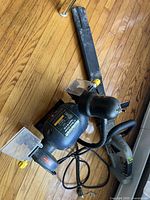 Mastercraft bench grinder with power cord, two grinding wheels, and attached work light and eye shields lying on a wooden floor.