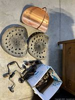 Top-down view showing two cast iron tractor seats, two hand crank drills, some roller skate attachments in a box, and the copper firewood caddy