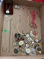 Full overview of costume jewelry lot showing chains, necklaces, pins, brooches, earrings, and prayer locket in box
