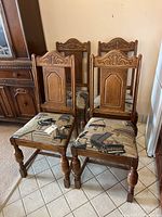 Four solid oak dining chairs with carved backs and piano theme fabric upholstery, arranged in a group.