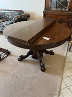 Side view of round table top with one leaf installed, showing pedestal base and carved feet