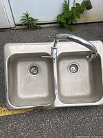 Top view of double bowl stainless steel sink with drain strainers and mounted chrome faucet tap.
