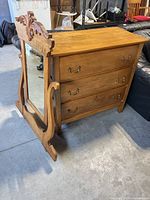 Side angle view showing dresser body and attached swing mirror with carved wooden frame.