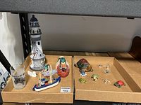 Overview of all items in the lot showing lighthouse figurine, carved and ceramic ducks, fishing troller model, and collection of turtles on cardboard boxes.