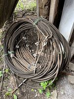 Coils of heavy metal cable with cable clamps and loops, bundled together with ties, placed outdoors near wooden structures.