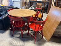 Round wood top kitchen table with four red wooden chairs and the rectangular leaf standing against the side.