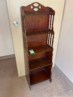 Front view of antique wooden knickknack shelf, showing four shelves and decorative top cutout design
