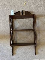 Full view of dark wooden wall-mounted shelf with three shelves and decorative top finial.