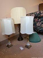 Three table lamps: one tall brass lamp with beige shade, two smaller matching brass and marble base lamps with white scalloped fabric shades. A green pleated fabric lamp shade is also present.