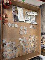 Overview of assortment of Canadian coins and two one dollar banknotes in a cardboard box, showing various pennies, nickels, silver dollars and 50 cent pieces.