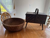 Wooden accordion-style sewing caddy with handle and legs next to a large round woven basket on a wooden table