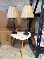 Photo of the side table with two brown metal base table lamps with beige shades on top, showing overall lot contents.