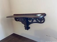 Side view of the ornate wooden wall shelf showing carved bracket detail and wall mounting.