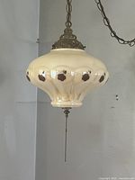 Full view of the vintage swag lamp hanging from a chain, showing the iridescent cream-colored glass shade with brown floral details.