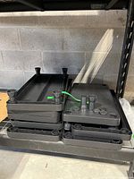 Stack of 8 black resin/plastic shelves with cylindrical posts for stacking, showing the side and top view of the shelves with connectors visible.
