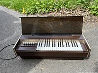 Front view of the Magnus Model 168 electric cord organ showing 25 keys and 6 control switches on the left, with a translucent brown plastic top lid raised.