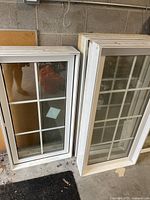 Two white vinyl windows leaning against a concrete wall with colonial grid.