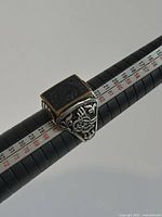 Close-up front angled view of the sterling silver men's ring on a ring sizer, showing detailed filigree on the side and black square centerpiece.