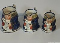Front view of three Allertons porcelain Toby Jugs showing character faces, blue coats, beige hats, and red accessories.