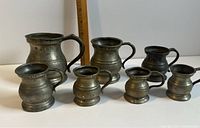 Set of seven pewter baluster tankards arranged showing size differences and features