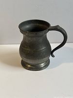 Front angle view of antique pewter tankard showing shape and handle detail.
