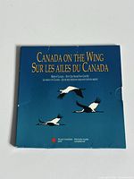 Photo of closed blue folder packaging titled 'Canada on the Wing / Sur Les Ailes Du Canada' by Royal Canadian Mint showing slight wear.