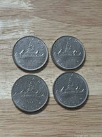 Four Canadian one dollar coins placed on a wooden surface, showing reverse side with canoe design and dates 1968 and 1984.