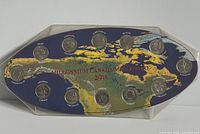 Front view of the Millennium Canada Quarters set showing 12 quarters mounted in a leaf-shaped display holder with a color map of Canada.