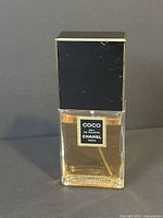 Front view of rectangular glass perfume bottle filled with light amber liquid, black cap top with Chanel logo on label.